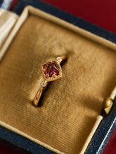 The CAMELLIA 14K Solid Gold Carena Garnet Ring, adorned with small clear stones, is elegantly displayed in a velvet-lined ring box.
